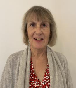 Glenda Norquay - middle aged Caucasion women with chin-length ash blonde hair wearing an oatmeal-colored cardigan over red print shirt