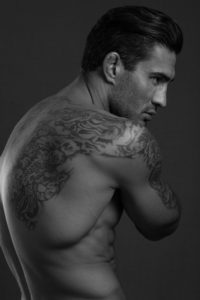 White male nude in profile from waist up with tatoos on back